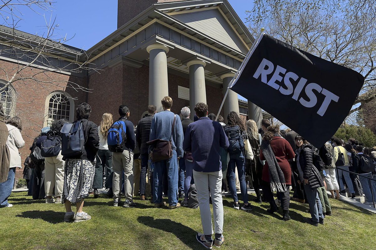 Harvard University community members, one with a 'resist' flag, gather at a rally on campus 
