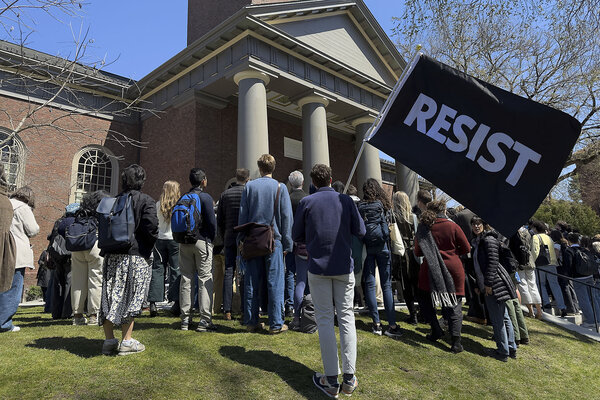Harvard University community members, one with a 'resist' flag, gather at a rally on campus 